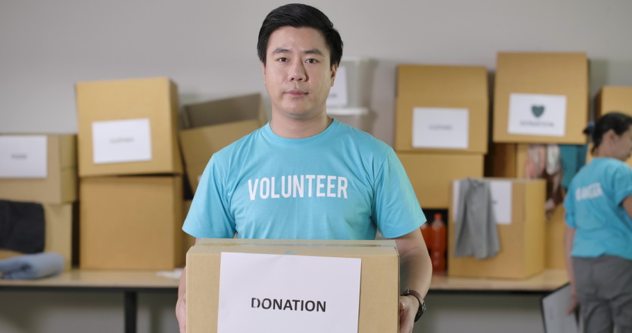 Confident young asian male volunteers looking at camera talking about the charity work and invite people to join with his community or donate things to the poor during the Coronavirus pandemic. Royalty-Free Stock Footage #1055951354