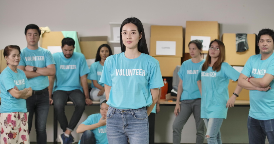 Close-up portrait of confident young asian woman volunteers looking at camera and posing with attractive smile in front of the charity workers team in background. Social support and donation concept. Royalty-Free Stock Footage #1055951366