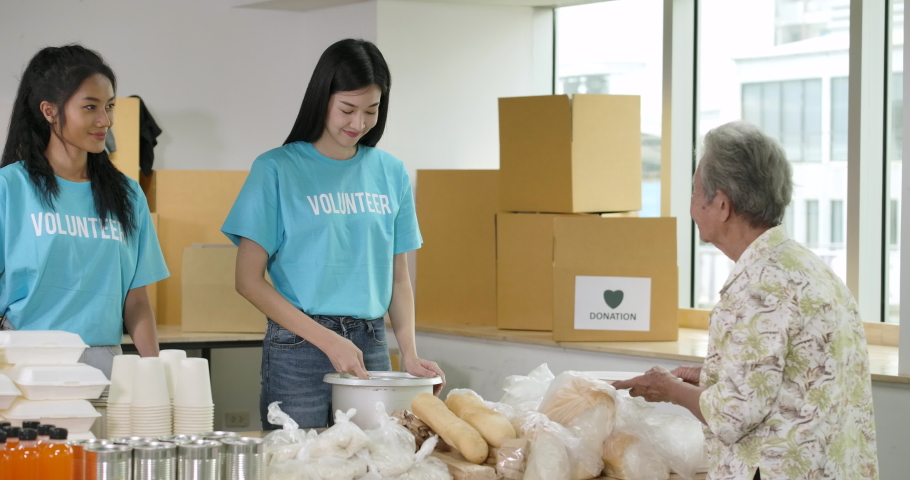 Group of Young asian male and female volunteers putting food on the plate and serving at homeless shelter as charity workers and members of community work to the poor during the Coronavirus pandemic. Royalty-Free Stock Footage #1055951444
