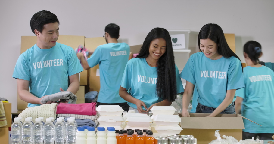 Young asian male and female volunteer putting food in a donation box together as charity workers and members of the community work to the poor during the Coronavirus pandemic. social distance concept. Royalty-Free Stock Footage #1055951456