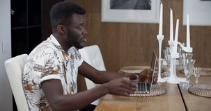 A young African American man sits indoors and communicates via video communication on a laptop. Man portrait