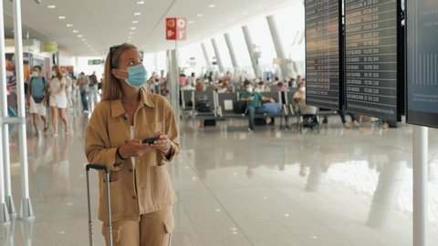 Woman tourist travel by plane, airport terminal timetable, wearing protective medical mask. Girl post covid, open boarders after lockdown, coronavirus pandemic