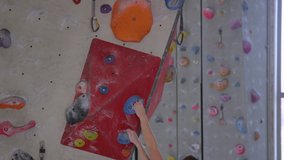 SLOW MOTION, CLOSE UP: Girl loops her belay rope into a carabiner while holding on to a pocket hold on the side of a red volume. Experienced rock climber trains lead climbing in an indoor center.