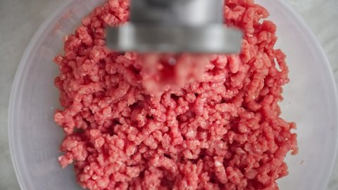 Electric mincer machine closeup. Filling comes out through meat grinder sieve. Grinder with fresh chopped meat. Process of raw meat grinding in kitchen with mincing machine. Preparation of minced beef