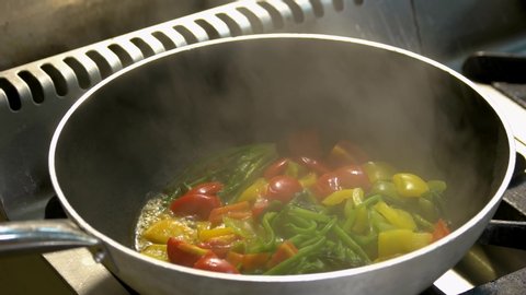 Close up chef cooking vegetables in pan. Mixed vegetables being stewed in a frying pan. Food cooking concept.