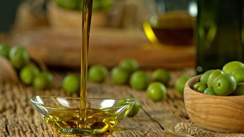Super Slow Motion Shot of Pouring Fresh Olive Oil into Glass Bowl on Old Wooden Table at 1000 fps.