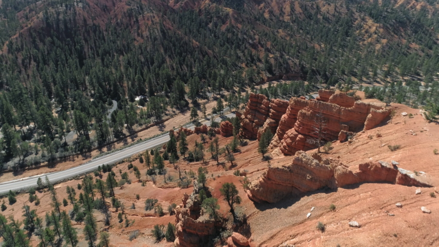 4K drone view on the abstract spire-shaped reddish rock formations hoodoos at Bryce canyon. Beautiful aerial view on the road in the scenic landscape with pine woods. Wild nature view. Utah, USA