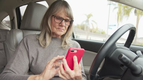 Senior Caucasian woman driver text messaging or checking map app on her smartphone while in parked car. Older white retired woman using smartphone before driving. Slow motion 4k