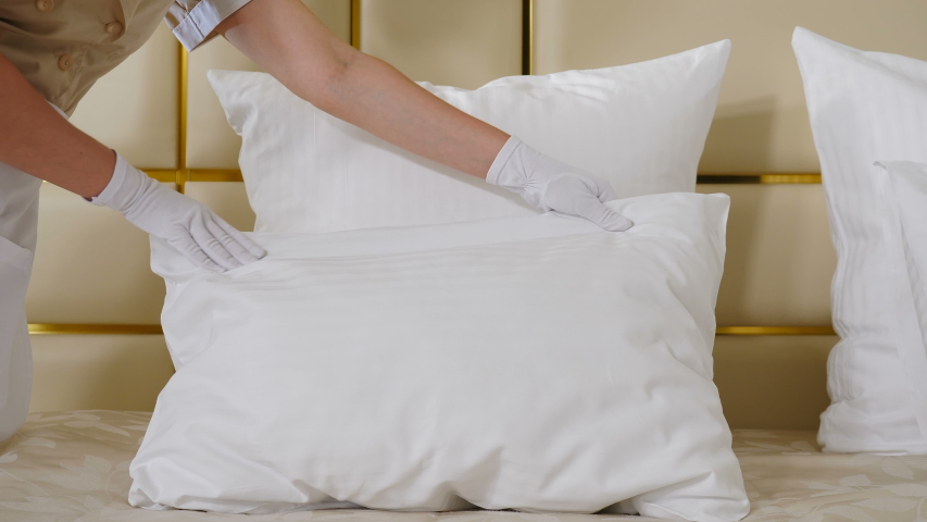 Hotel cleaning concept. Close-up view of young pretty maid in uniform making bed in room touching pillows punching into shape. Preparation of hotel room. 4 k video Royalty-Free Stock Footage #1055964281