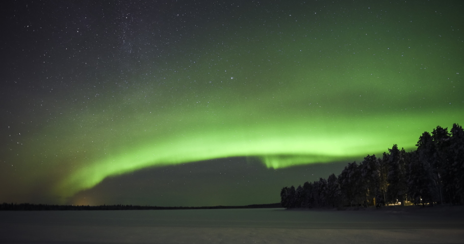 Northern lights timelapse of bright green aurora borealis in the night sky, with stars. Time lapse over remote landscape of frozen lake and forest in Lapland, Finland