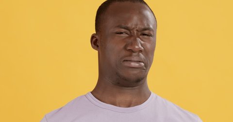 Disgusted african american man feeling aversion, frowning nose, yellow studio background