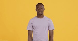 Peace for you. Cheerful african american guy gesturing V-sign and smiling, yellow studio background