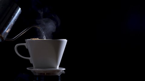 Hand Drip coffee, pouring hot water over roasted. Man pouring water from the coffee pot into the paper filter. Black Background. Side View