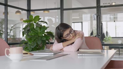 A beautiful and attractive office female or girl employee with eyeglasses exhausted and tired sleeping or taking a nap on a desk during office or working hours in a modern corporate start up space. 