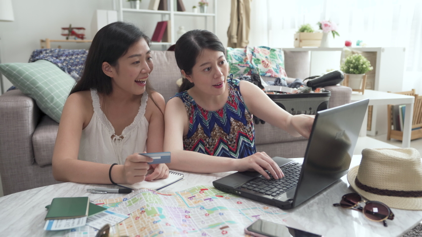 two asian japanese girl friends sitting on floor in house living room searching internet for summer break travel trip. ladies holding credit card buying cheap airplane ticket on internet. e commerce.