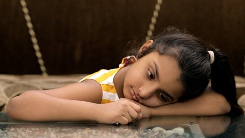 Closeup shot of a cute little girl leaned against a table - boring lifestyle concept. Portrait shot of a bored Indian kid sitting alone during the home quarantine due to the outbreak of coronavirus