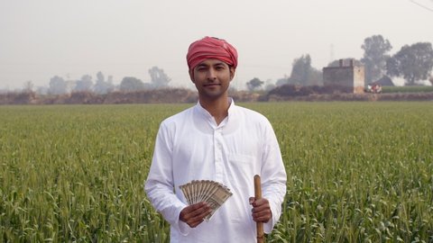The middle-aged Indian farmer is smiling while showing his monthly income. Handsome agricultural laborer in white kurta pajama holding five hundred rupees banknotes - financial concept