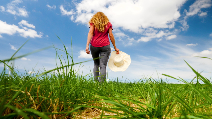 woman walking in green grass with cloud and blue sky
