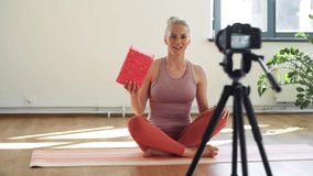 fitness, sport and video blogging concept - woman or blogger with camera on tripod and exercise block recording online yoga class in gym or studio