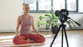 fitness, sport and video blogging concept - woman or blogger with camera on tripod recording online yoga class in gym or studio