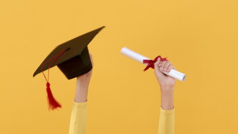 Hands holding square academic cap and degree paper roll celebrating graduation on yellow background 