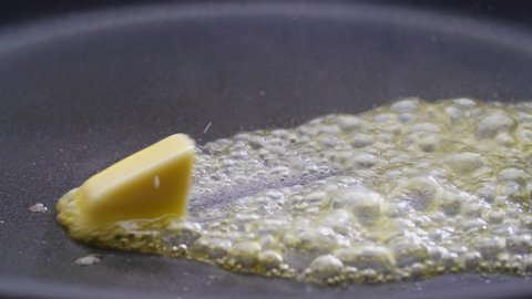 Butter melting sizzling in frying pan on stove. Close up.