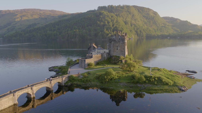 Aerial drone shot tracking around the stunning Eilean Donan Castle in Scotland, with the lake surrounding it and mountains in the background, and the reflection in the water. Royalty-Free Stock Footage #1055982527