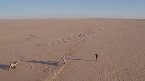 Aerial drone tracking shot of lone motorbike rider racing in the Dakar Rally or Africa Eco Race speeding into the desert with dust and smoke trails