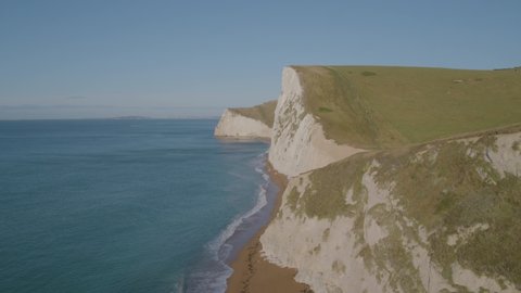 Aerial drone shot flying fast towards and past dramatic white chalk cliffs  on coast in England on a bright warm sunny day with a blue sky