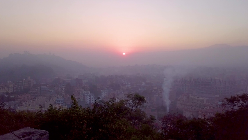 Aerial drone shot flying over Kathmandu, Nepal towards the sunrise on a mist hazy morning, with smoke rising from the houses below