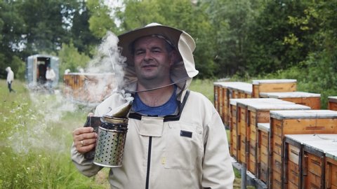 Portrait of experienced positive beekeeper with smoke hive tool in the farm garden. Apiarist. Apiculture. Professional. Beekeeping business.