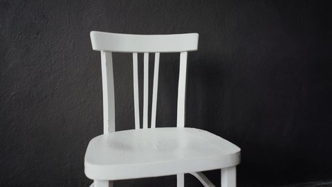 Against the grey wall stands an old white chair. Close-up
