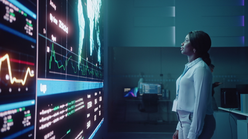 Young Female Computer Science Engineer Looking at Big Screen Display Showing Global Map with Data Points. Telecommunications Technology Company System Control and Monitoring Room with Servers. | Shutterstock HD Video #1055986655