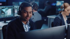 Close Up Portrait of a Joyful Technical Customer Support Specialist Talking on a Headset while Working on a Computer in a Call Center Control Room Filled with Computer Display Screens and Data Servers - Powered by Shutterstock - Get 15% off with code: PIKWIZARD15