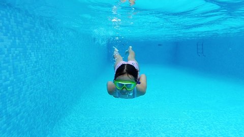 Slow motion view little 7 - 8 years old girl wear swimsuit and goggles submerged in water enjoy summer vacations swimming in pool. Active lifestyle and sport activity concept