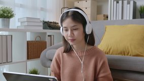 Young Asian woman wearing headphones and using digital tablet with video call online on internet to friend.