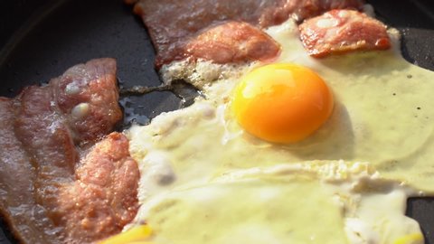 egg and bacon are cooked in a pan. In a hot pan two pieces of bacon and egg, close-up. Breakfast in the sunlight