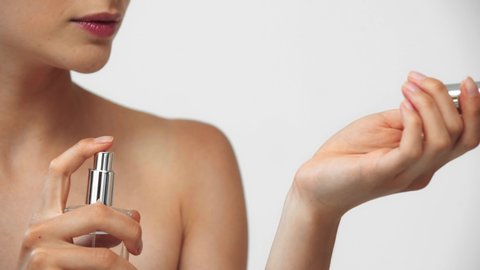 Naked woman spraying perfume on hand and smiling isolated on grey