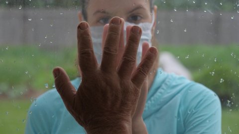 Woman in protective medical mask and illness old man touch their hands through glass window that separates them from each other. Quarantine for coronavirus pandemic. Hope hand and support for recovery