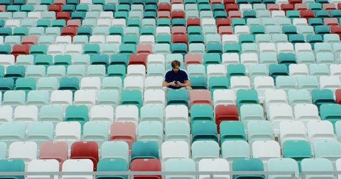 View of a lonely fan spectator using phone to make a bet during sports event on an empty stadium. Isolation, events during coronavirus pandemic concept