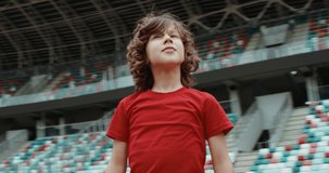 Cute little kid boy soccer player spreading hands on an empty stadium, dreaming of becoming professional player, soccer star. RED cinema camera RAW graded footage