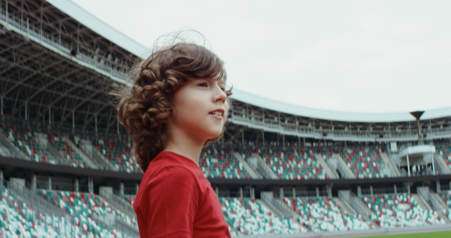 Cute little kid boy soccer player standing on an empty stadium, dreaming of becoming professional player, soccer star. RED cinema camera RAW graded footage Royalty-Free Stock Footage #1055995298