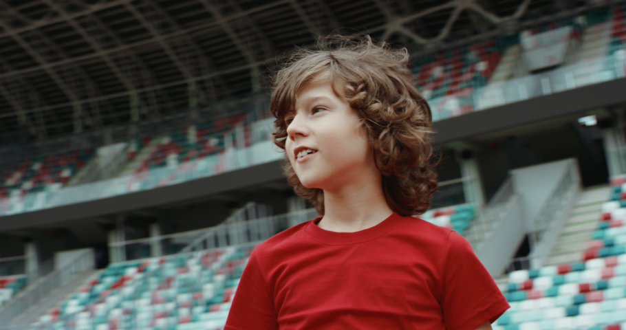Cute little kid boy soccer player standing on an empty stadium, dreaming of becoming professional player, soccer star. RED cinema camera RAW graded footage | Shutterstock HD Video #1055995298