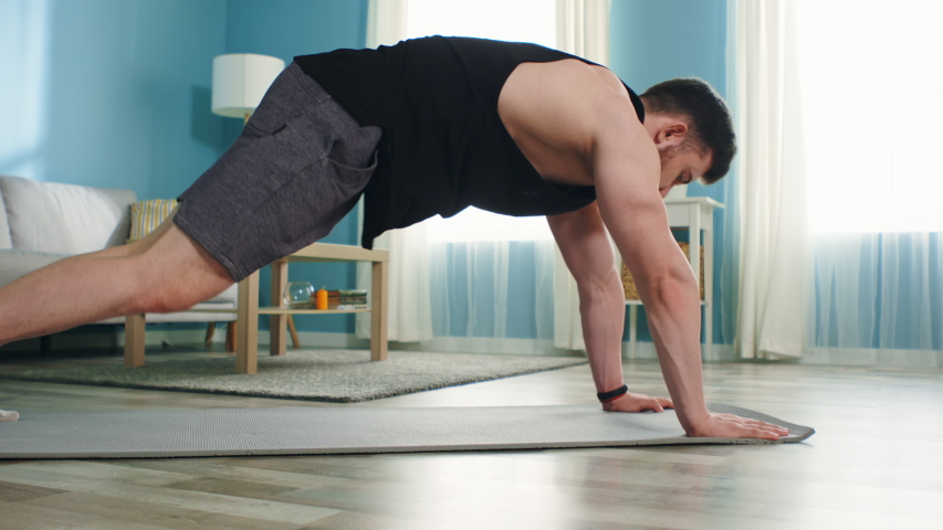 Young athletic man is training at home, using gadget, doing mountain climber exercise, working hard to maintain body shape in isolation, Zoom out, Slow motion. Royalty-Free Stock Footage #1055996837