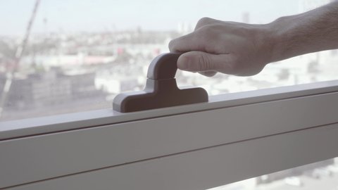 Hand opens an office window with handle in skyscraper or tall business building. Twist handle. High riser of big cooperation or school facility. Modern meeting room glass window with view to the city