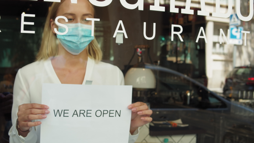 cafe or restaurants and business reopen after coronavirus quarantine is over.  Woman with face mask turning a sign on a door shop. small business after covid lockdown. Spain, barcelona Royalty-Free Stock Footage #1056003665