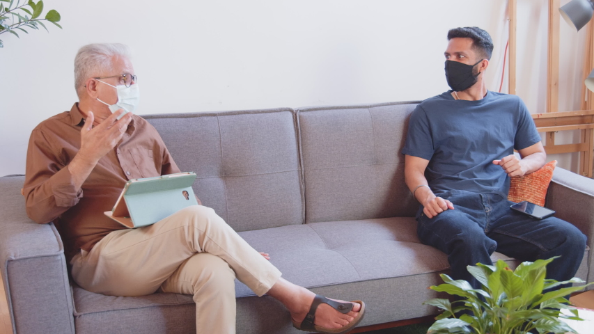 Two colleagues social distance on a couch at work while wearing masks and using their phones Royalty-Free Stock Footage #1056005168