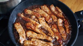 Delicious pork strips cooking in caramel sauce for dinner.Tasty natural meat ingredients stewed in hot pan.Spicy beef stripes cooked for lunch in close up video clip