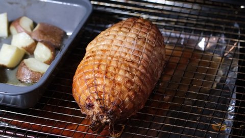 Meat thermometer being inserted in hot round roast on wire wrack in oven with cut up potatoes cooking in pan beside roast