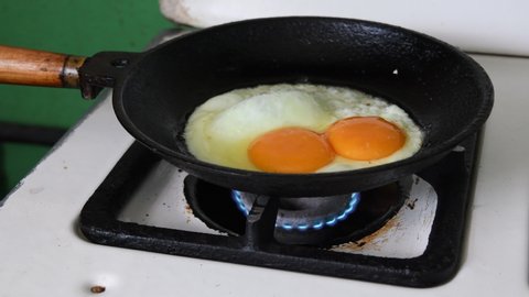 Huge chicken egg with two yolks frying in old cast pan on flaming gas fire of kitchen stove. Tasty homemade organic food